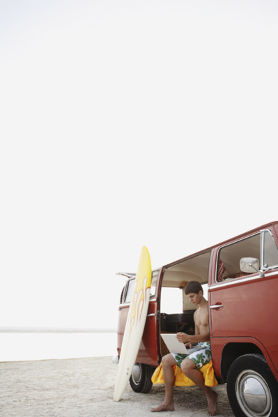 Young surfer using laptop in van on beach. Date : 2008