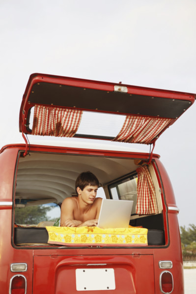 Young surfer using laptop in van on beach. Date : 2008