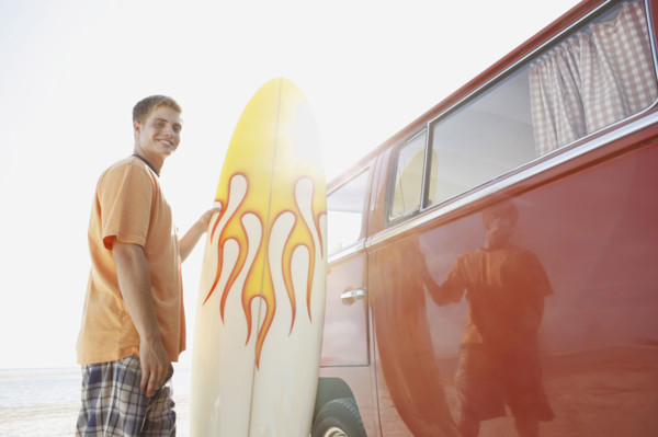 Portrait of young man holding surfboard near van. Date : 2008