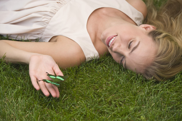 Woman laying on grass holding green butterfly.