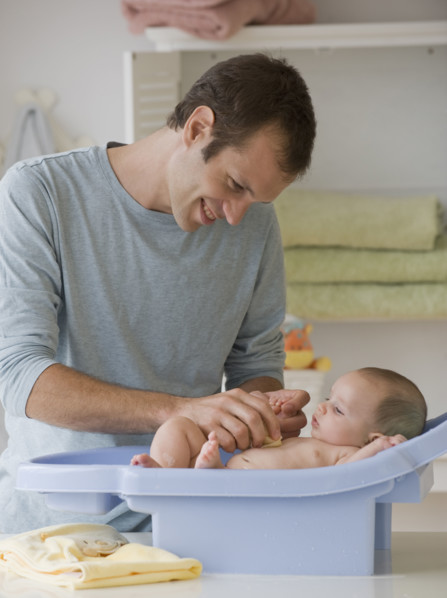 Father bathing baby son in baby bathtub.
