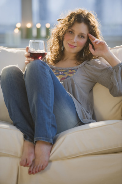 Portrait of woman with red wine sitting on sofa.