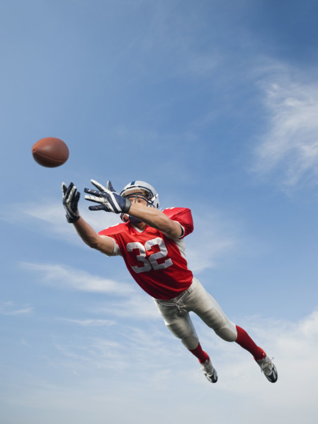Football player in mid-air reaching for football. Date: 2008