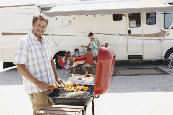 Man barbecuing with family and motor home in background. Date : 2008