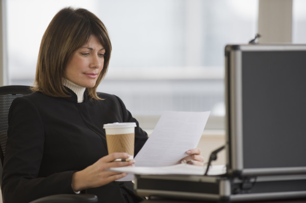 Businesswoman holding coffee and reading paperwork.