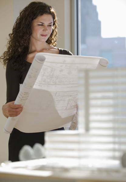 Architect viewing blueprints near building model.