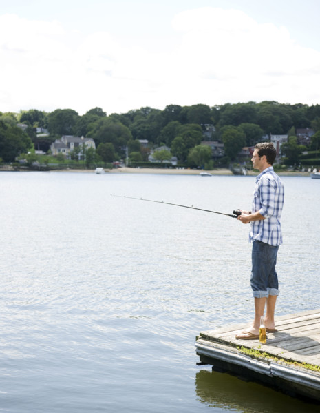Man fishing off dock with beer at feet. Date: 2008
