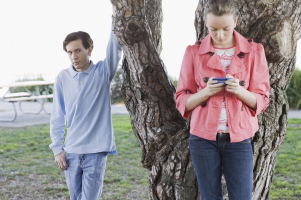 Boy watching girl text messaging outdoors. Photographe : PT Images