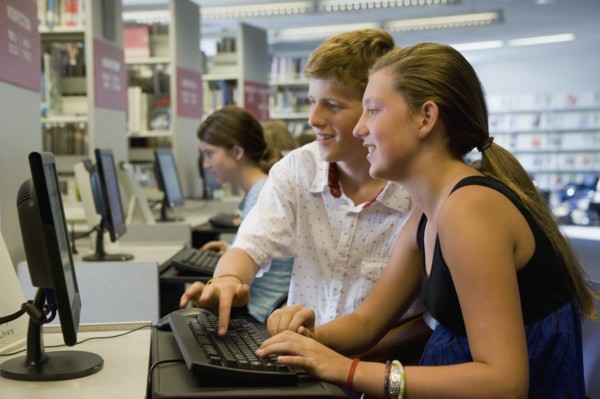 Teenagers using computer in library. Photographe : mark edward atkinson