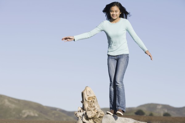 Teenage girl balancing on driftwood. Photographe : PT Images