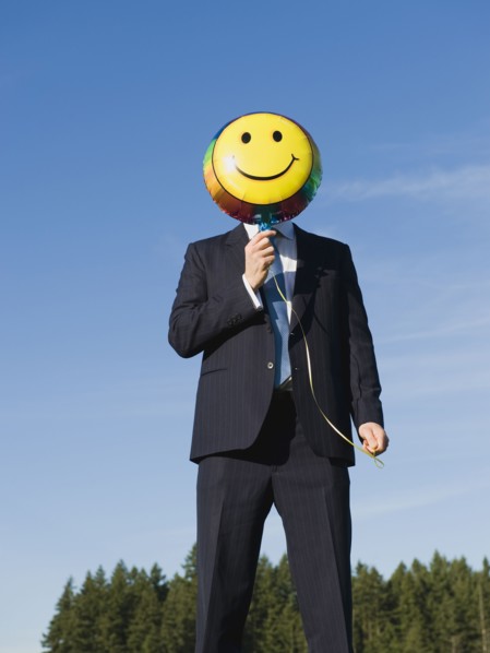 Businessman holding smiley face balloon over face.