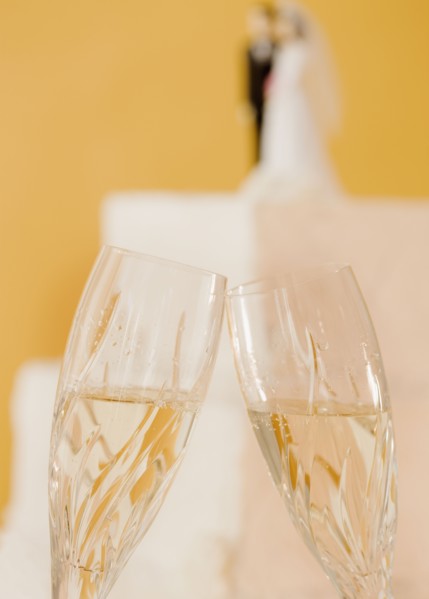 Close up of toasting champagne glasses and wedding cake. Photographe : Jamie Grill