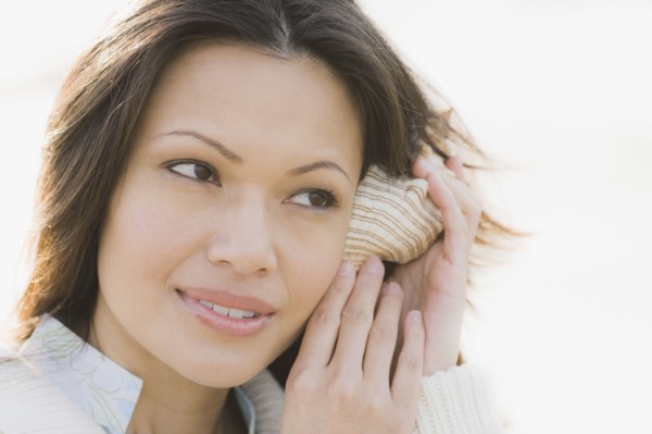 Close-up of woman listening to shell. Photographe : PT Images