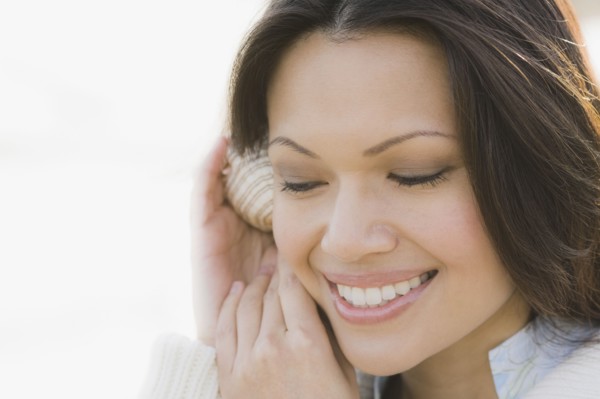 Close-up of woman listening to shell. Photographe : PT Images
