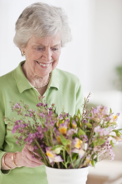 Senior woman setting flowers in vase.