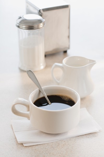 Cup of coffee with milk and sugar on table.