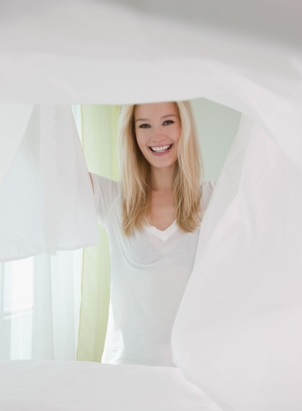 Portrait of young woman making bed. Photographe : Jamie Grill