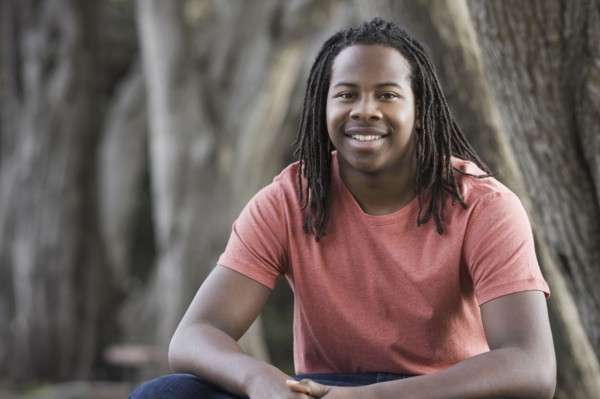 Portrait of teenage boy (16-17) with dreadlocks, sitting in park. Photographe : PT Images