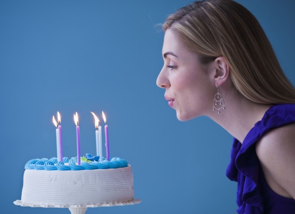 Young woman blowing candles on birthday cake, studio shot. Photographe : Daniel Grill