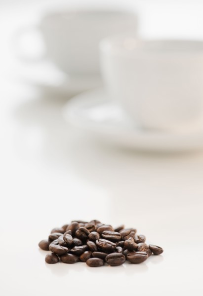 Heap of coffee beans with coffee cups in background.