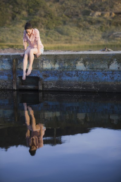 A woman sitting on a stone wall by water