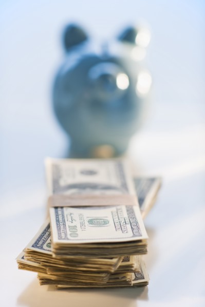 Bank notes and coins by a piggy bank.