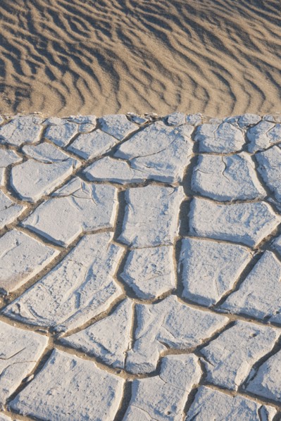 Sand dunes in the desert with cracked earth.