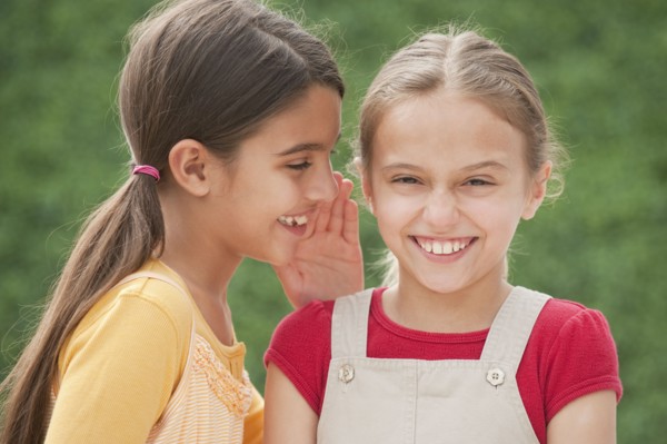 Two girl friends whispering.