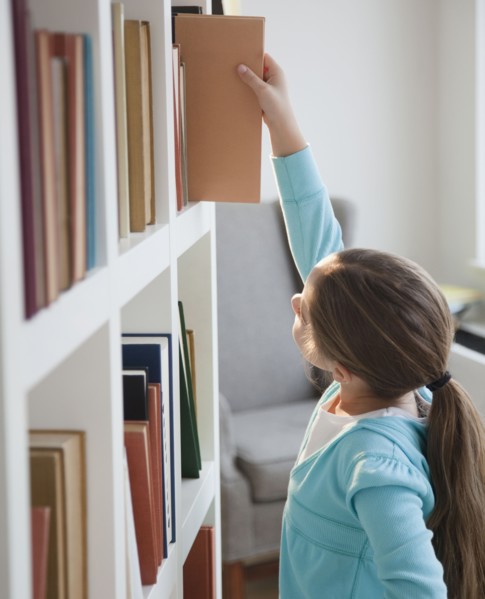 Young girl taking book of bookshelf. Photographer: Jamie Grill