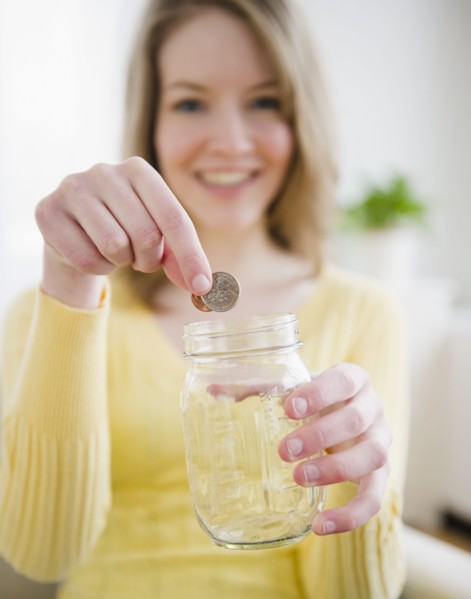 Woman putting coins in a jar. Photographe : Jamie Grill