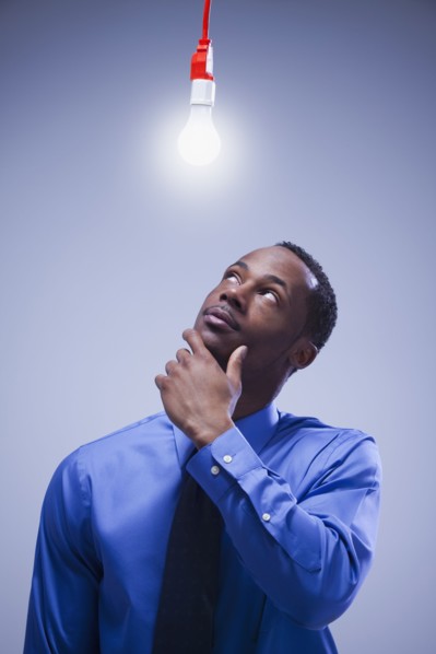 Contemplative businessman standing under a light bulb. Photographe : Mike Kemp