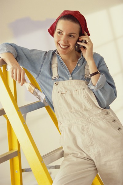 Woman talking on phone while painting her home. Photographe : Rob Lewine