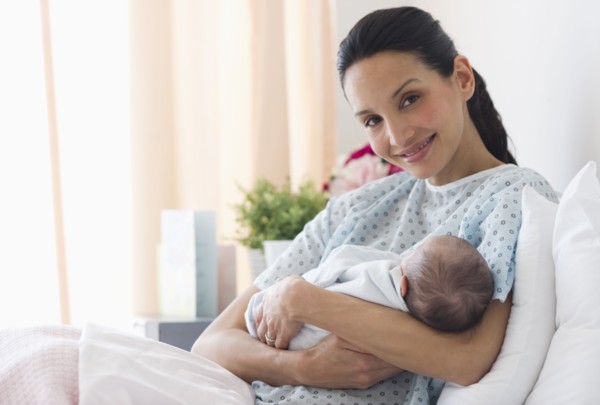 Mother holding newborn baby in hospital bed.