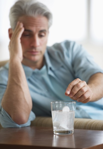 Man with a headache putting medicine in glass of water.