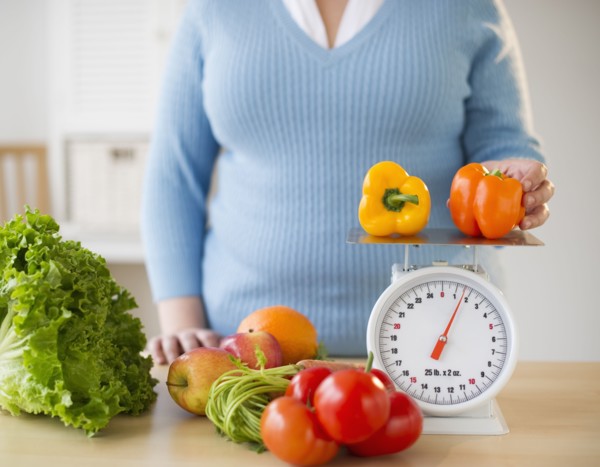 Overweight woman measuring peppers on a food scale.