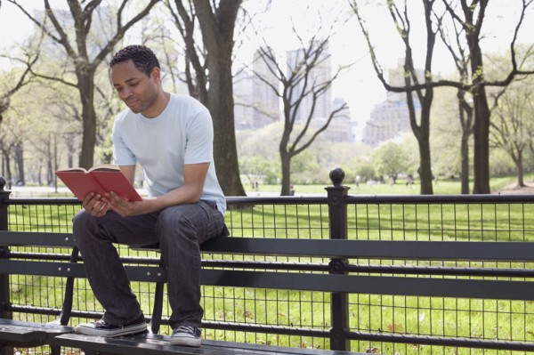Man sitting on bench reading book in Central Park. Photo : David Engelhardt