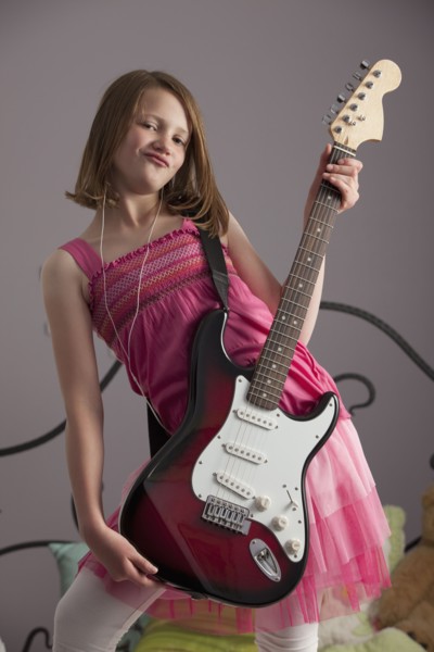 Young girls playing guitar on her bed. Photo : Mike Kemp
