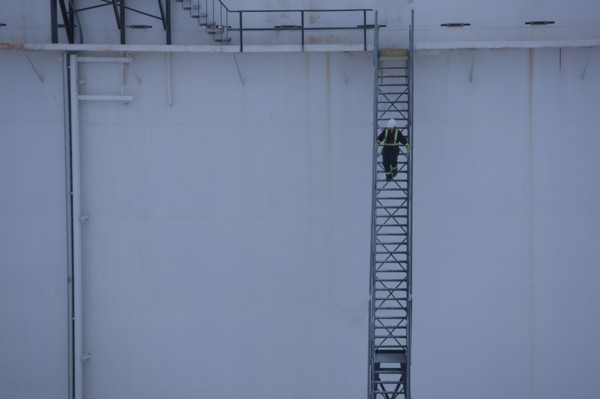 Worker walking down stairs on an oil tank. Photo : Dan Bannister