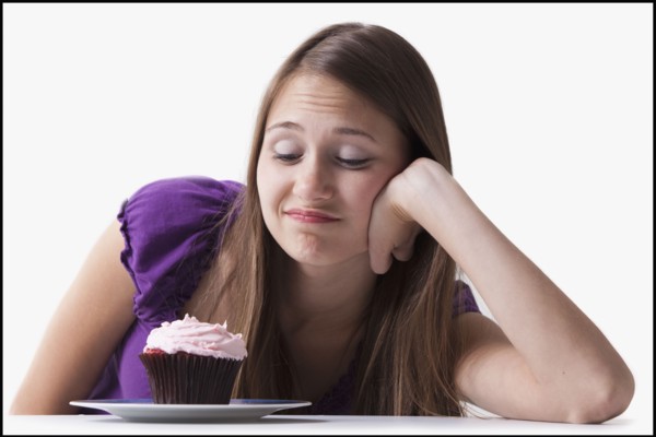 Woman with a sweet tooth resisting a cupcake. Photo : Mike Kemp