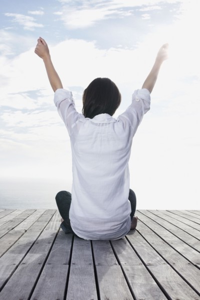 Woman sitting on porch with her arms raised. Photo : momentimages