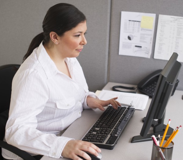 Businesswoman working on laptop in cubicle.