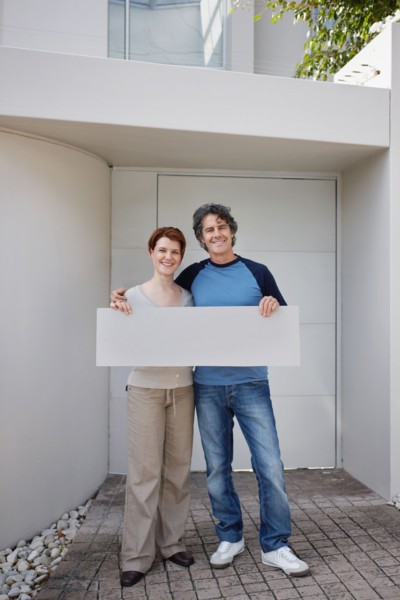 Couple standing in front of their home. Photo : momentimages