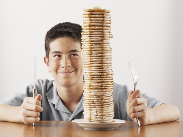 Young boy sitting behind a tall stack of pancakes. Photo : FBP