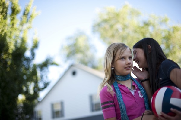 Young girl whispering to her friend. Photo : Tim Pannell