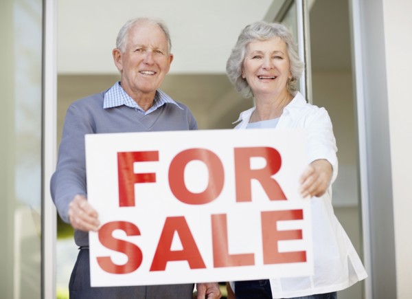 Senior couple holding for sale sign. Photo : momentimages