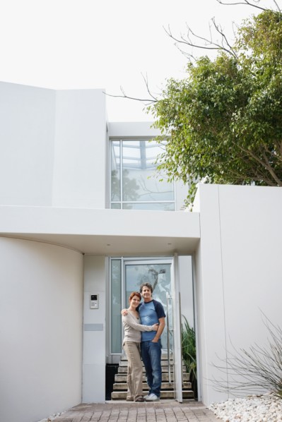 Happy couple embracing in front of their home. Photo : momentimages