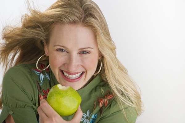 Happy blond woman eating an apple.