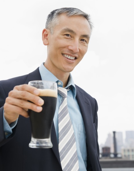 Businessman holding pint of ale and looking at camera. Photo : Jamie Grill