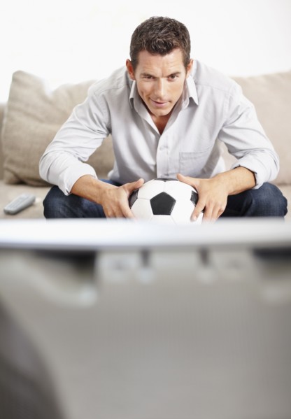 Mid adult man watching football match on television. Photo : Momentimages