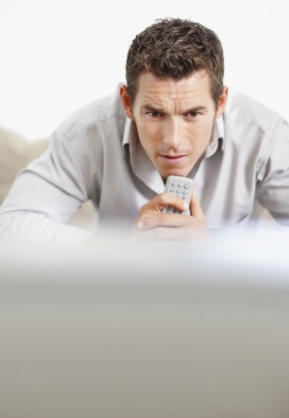 Tense man holding remote control in front of television. Photo : Momentimages